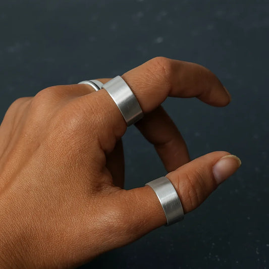Hand wearing two RajBand 999 purity silver rings on a dark background