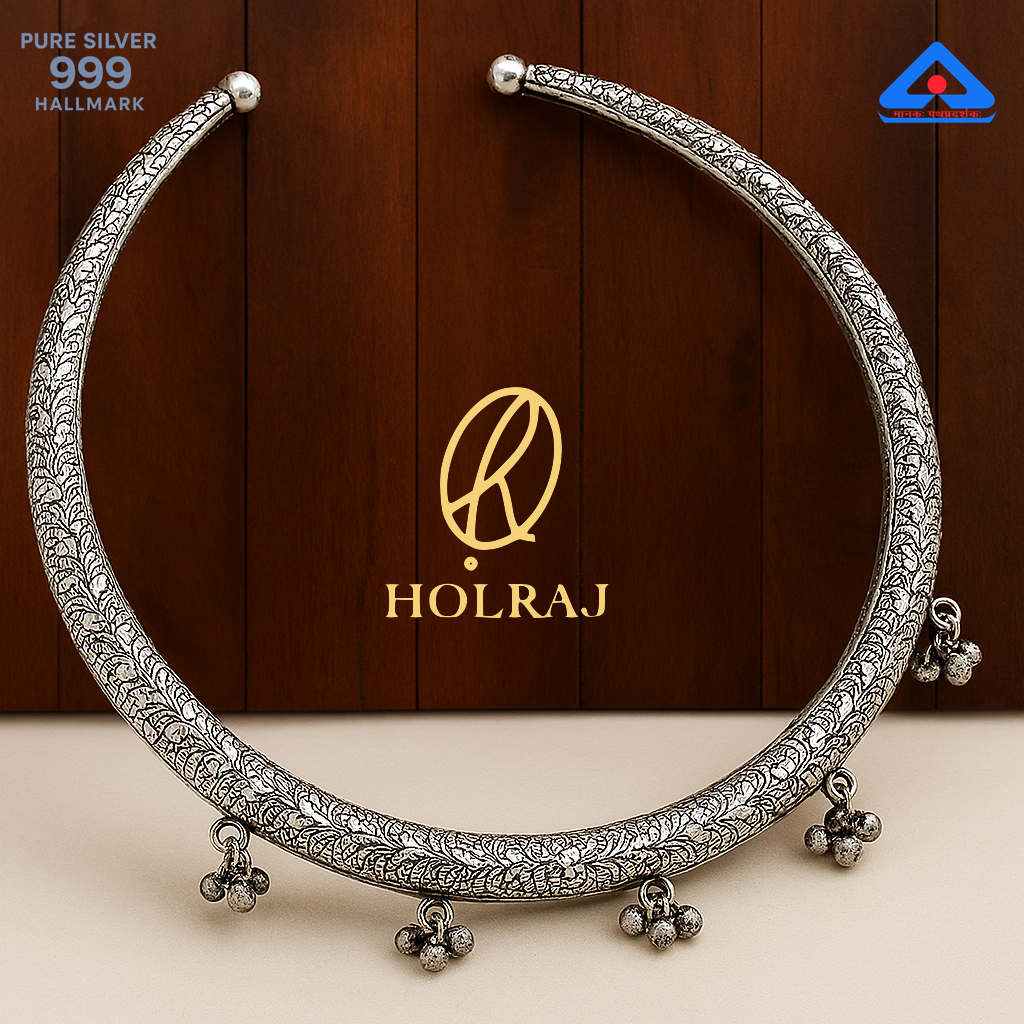 Close-up of a handcrafted 999 silver Hansuli necklace with embossed patterns and ghungroos, placed against a wooden background by Holraj