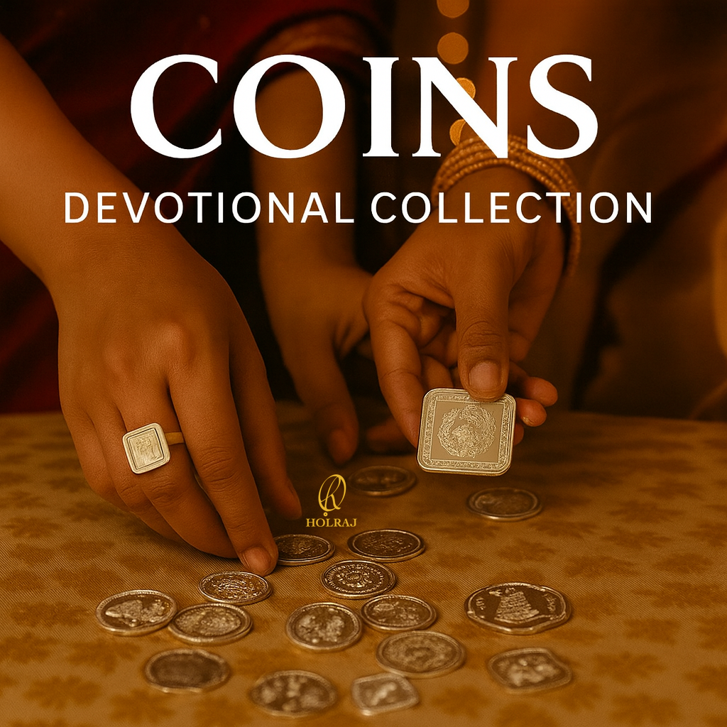 Two women dressed in festive Indian attire pick up silver coins with devotional engravings from a table during a celebration. Multiple coins are scattered across a golden-patterned surface. Text reads “COINS – DEVOTIONAL COLLECTION."