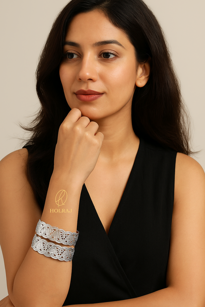Woman wearing a black sleeveless top with Pair of high-polish BIS Hallmark 999 pure silver bangles or kada with intricate triangular cutwork, set against a beige background with Holraj branding.