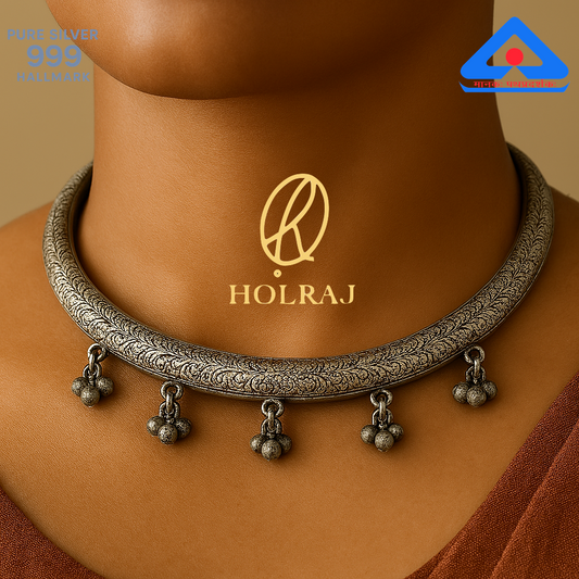 Close-up of a holraj branded handcrafted 999 silver Hansuli necklace with embossed patterns and ghungroos, placed against a wooden background.
