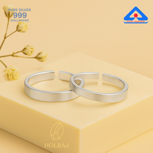 Two silver toe rings on a beige surface with 'HOLRAJ' branding and 'PURE SILVER 999 HALLMARK' text.