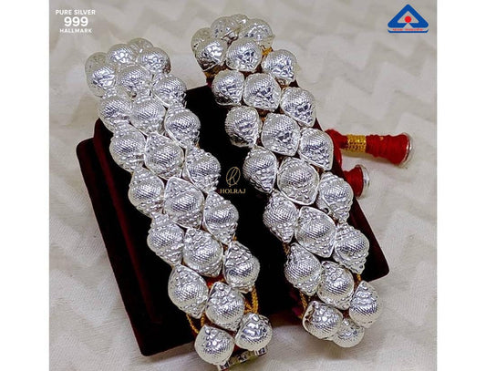 Pair of Shankh Ponchi bracelets in 999 pure silver featuring mirror-polished conch domes on red and gold thread, placed on a soft cream fabric background. By Holraj.